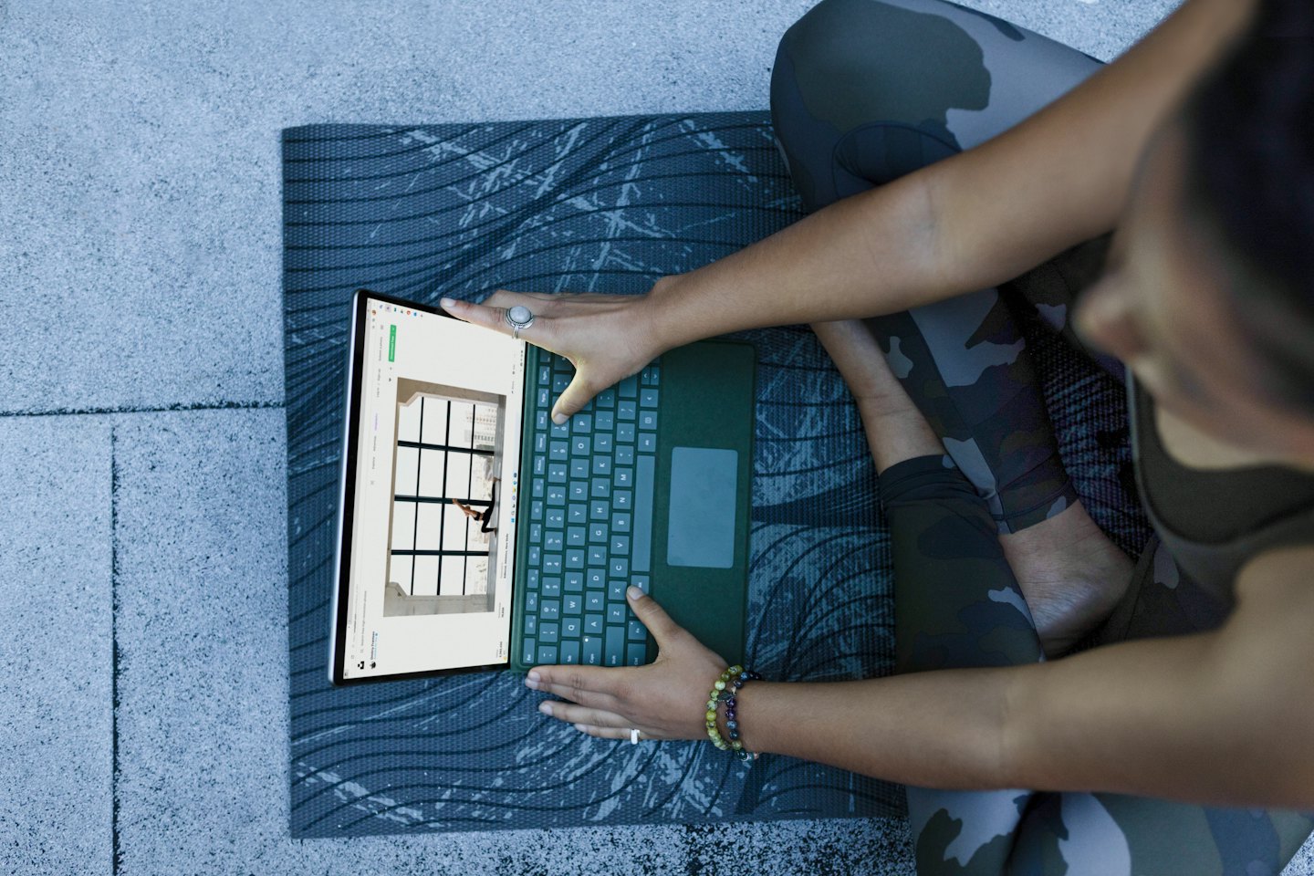 Eine Person sitzt auf einer Yogamatte und benutzt einen Laptop.